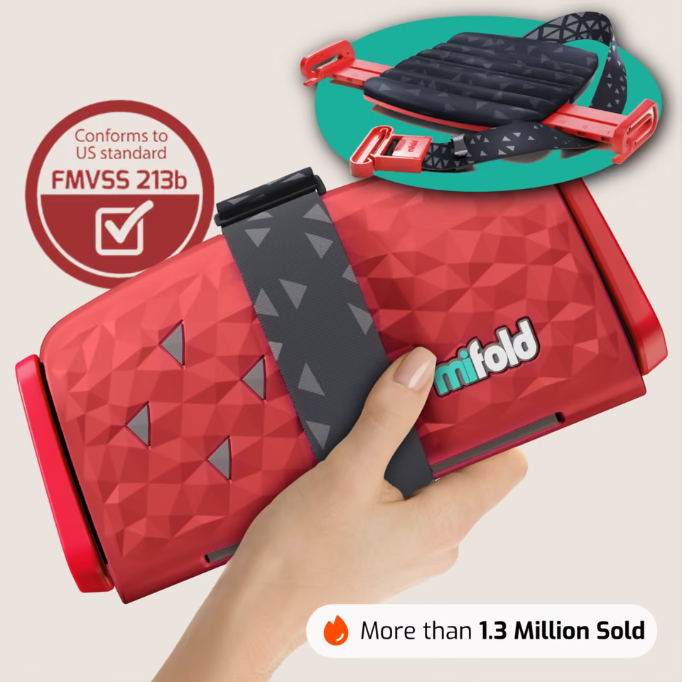 Mifold Comfort in Racing Red: folded booster held in one hand with its FMVSS 213b safety badge and 1.3 million sold proof